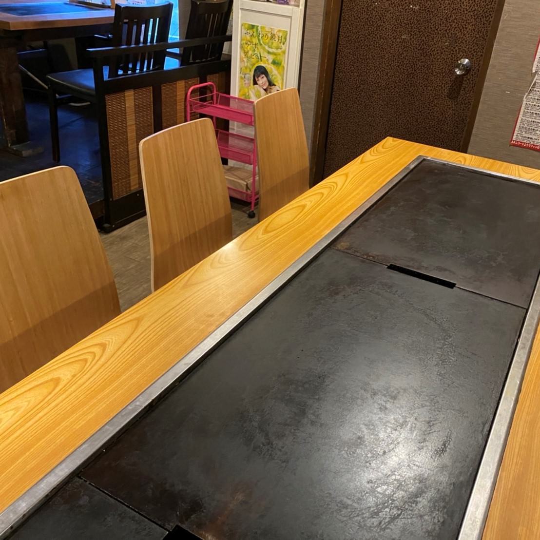 もんじゃ焼きやお好み焼きを楽しむための鉄板が設置されたテーブル。座席は木目調の椅子が並ぶ。