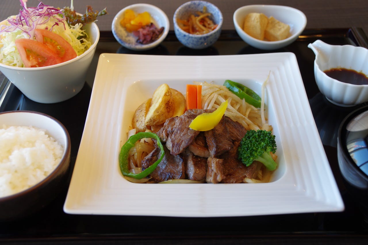 黒いお盆にごはんや副菜、焼肉がのっている