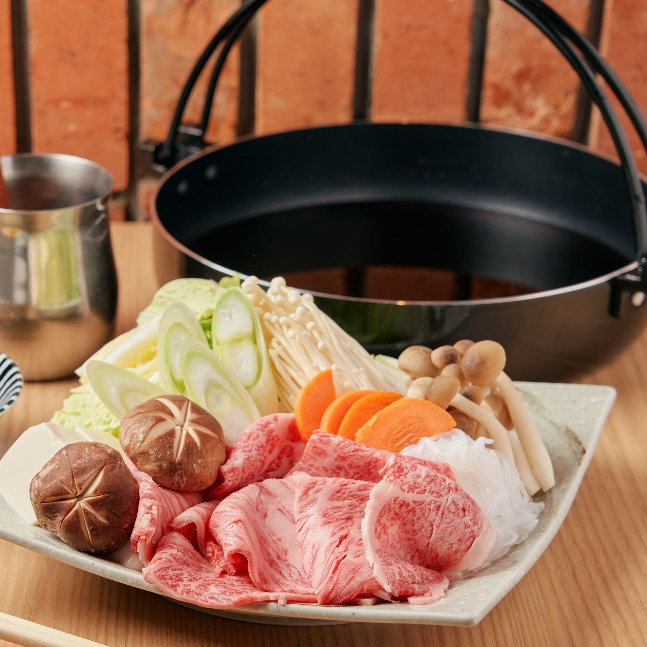 すき焼きの具材と鍋がベージュのテーブルに置かれた様子