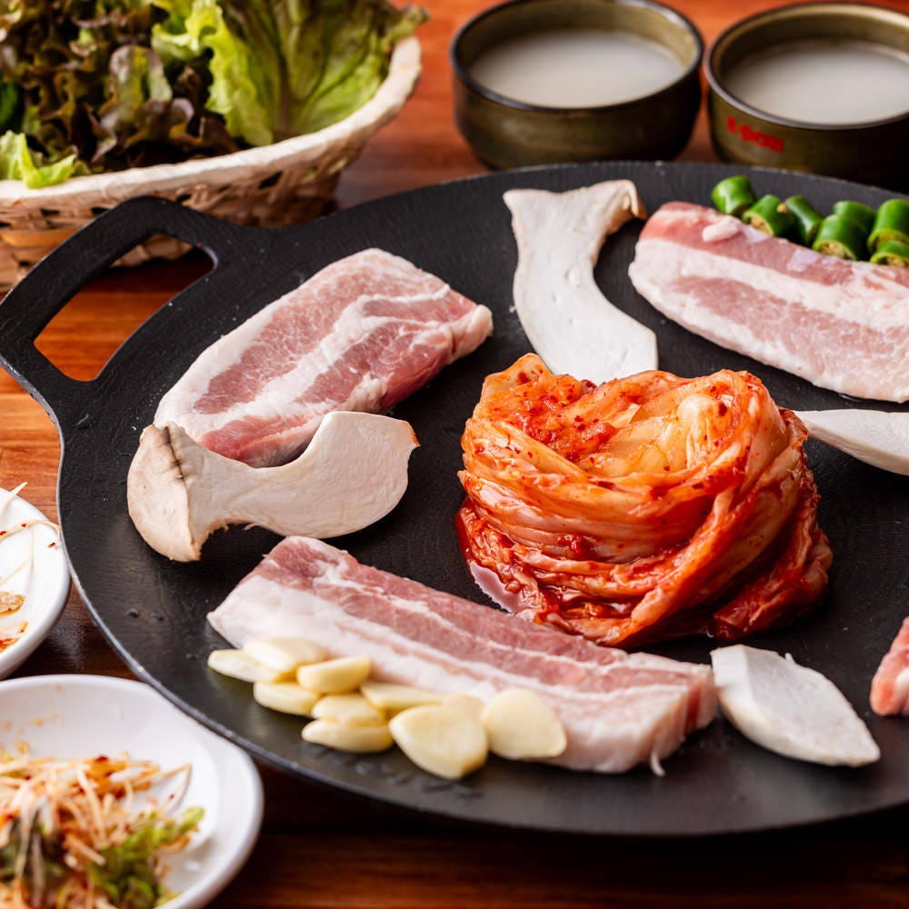 器に盛られたサムギョプサルセットとコップに入ったマッコリ